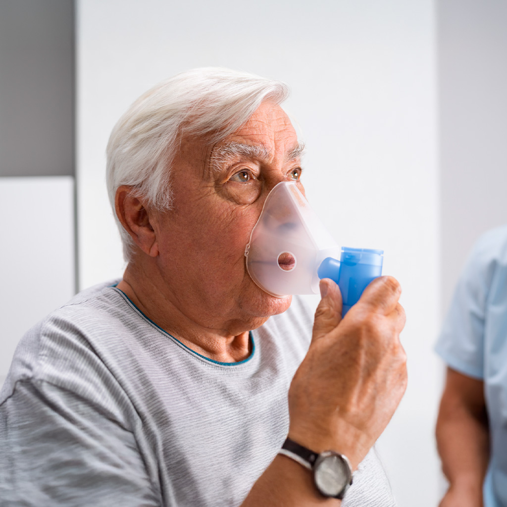 Homem idoso utilizando máscara de oxigênio para nebulização, ilustrando um momento de tratamento respiratório em ambiente domiciliar.