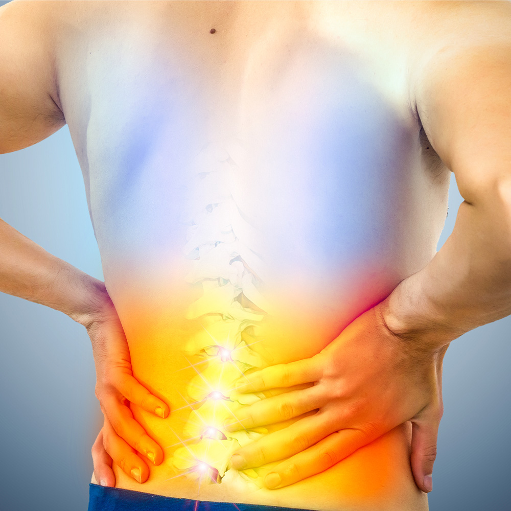 Pessoa com as mãos na região lombar das costas, com destaque colorido indicando dor ou inflamação na coluna vertebral.