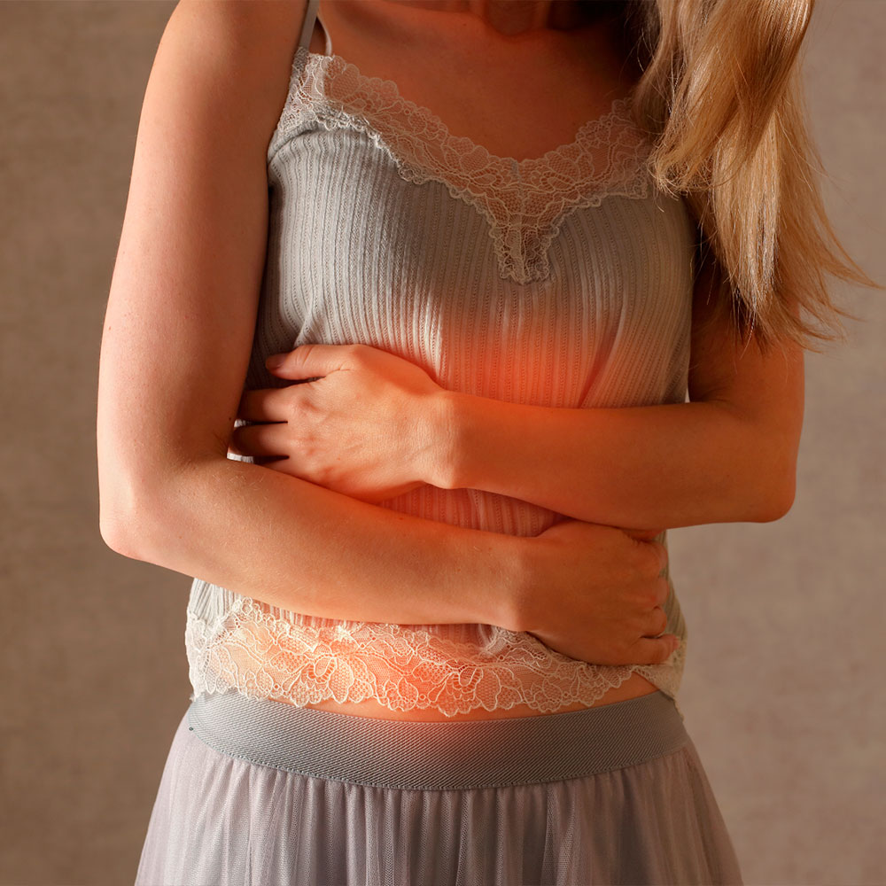 Mulher com as mãos sobre o abdômen, demonstrando dor ou desconforto abdominal, com área iluminada em vermelho simbolizando inflamação ou tensão.